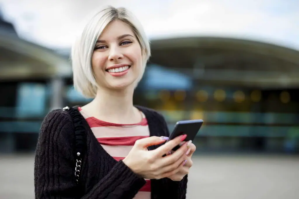 woman smiling while using mobile phone outside train station
