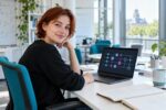 Junge Frau an einem Laptop mit schematischer Schaltkreisdarstellung.
